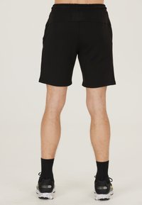 Zwarte sportshorts met een elastische tailleband en twee zijzakken, gecombineerd met zwarte sokken en hardloopschoenen met een gespikkelde zool.