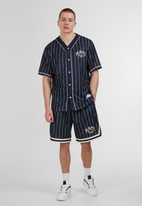 Camisa de botones de manga corta a rayas navy y pantalones cortos a juego, con detalles en blanco contrastantes y logo, fabricados en tejido ligero.