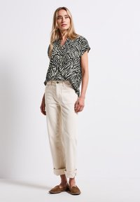 Blusa corta a maniche corte a righe zebra nera e crema, abbinata a jeans beige chiaro con risvolti e scarpe slip-on marroni. Tessuto morbido, vestibilità rilassata.