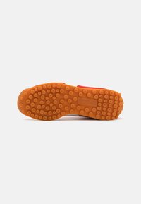 Red shoe sole with orange rubber, featuring circular traction patterns and a textured finish. The design includes a branded logo.
