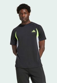 Černé sportovní tričko s limetkově zelenými a šedými detaily. Krátké rukávy, prodyšný materiál, s malým logem na levé hrudi.