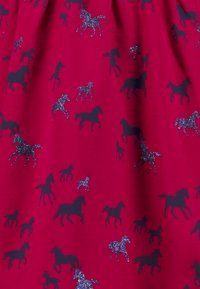 Roter Stoff mit einem verstreuten Muster aus schwarzen Pferden, von denen einige mit Glitzerdetails verziert sind, was einen strukturierten visuellen Effekt erzeugt.