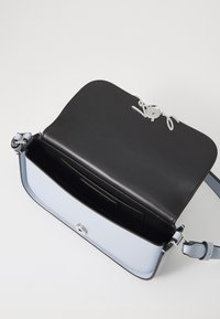 Světle modrá kožená taška přes rameno s černým interiérem, otevřený klapkový uzávěr zajištěný stříbrným kovovým zapínáním a značkovým kovovým detailem na okraji klapky.