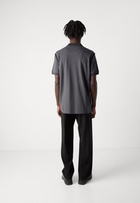 T-shirt gris à manches courtes avec un ourlet droit et des détails de couture discrets, associé à un pantalon large noir et des chaussures plates.