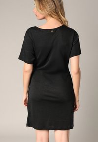 Robe noire à manches courtes avec une coupe décontractée, une texture douce, un col rond et un petit bouton décoratif au dos.