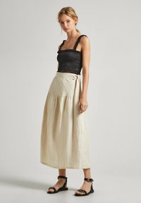 Svart smockad crop top med volangband och en lång beige randig kjol med en knytdetalj. I kombination med svarta sandaletter med remmar.