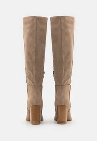 Beige suède kniehoge laarzen met een cilindrische, geribbelde houten hak en zijritsen. Glad textuur met een aansluitend ontwerp.