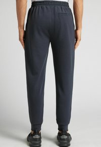 Mörkgrå sweatpants med resårmidja och smalnande mudd. Har en bakficka och mjuk textur. Bärs med svarta sportskor.