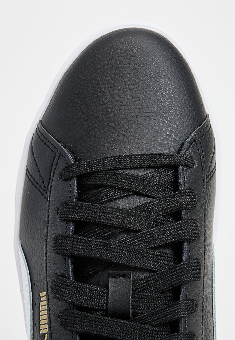Basket en cuir synthétique noir avec bout rond, surface texturée, lacets noirs et semelle en caoutchouc blanche. Logo Puma en doré sur le côté.
