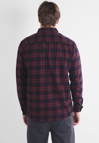 Chemise en flanelle à carreaux rouge et bleu marine avec manches longues et col. Elle présente un ourlet incurvé et des poignets à boutons.