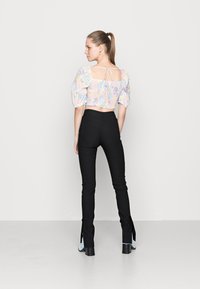 Top cropped com padrão floral em tons pastel, mangas bufantes e costas abertas. Calças pretas de cintura alta com fendas laterais e corte reto. Sapatos azuis de salto.