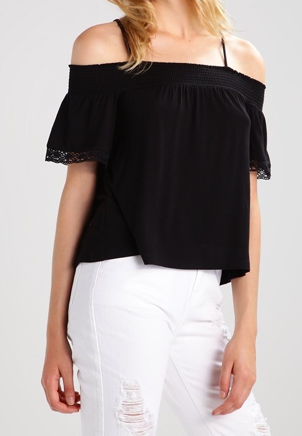Haut noir à épaules dénudées avec des manches volantes, corsage smocké et dentelle, associé à un jean blanc déchiré.