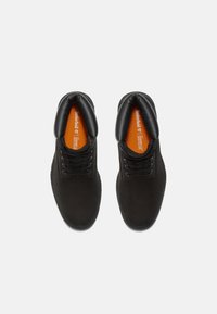 Bottines en daim noir avec un col rembourré, un design à lacets et une marque sur la semelle intérieure orange. Texture lisse et forme de bout arrondi.
