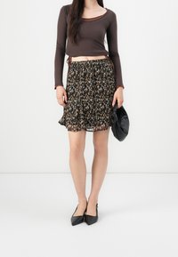 Braunes Langarmoberteil mit einem durchsichtigen Ausschnitt, kombiniert mit einem schwarzen Blumenkleid mit einem Rüschensaum. Schwarze spitze Ballerinas und eine schwarze Clutch.