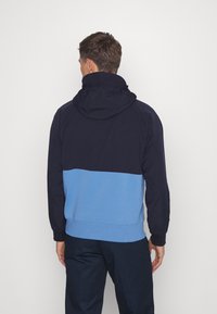 Herrtröja i marinblått och ljusblått. Har en justerbar huva, en färgblockdesign och ribbade cuffs vid handled och nederkant.