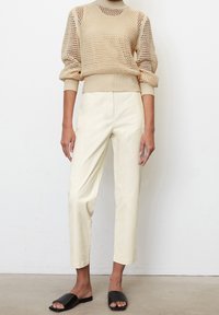 Beżowy sweter z dzianiny o fakturowanym wzorze, w połączeniu z kremowymi, zwężającymi się spodniami. Czarne klapki dopełniają całość.