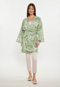 Zeleni kimono-stil ogrtač s bijelim uzorcima lišća, stegnut oko struka, u kombinaciji s laganim hlačama i bež cipelama. Glatka tekstura.