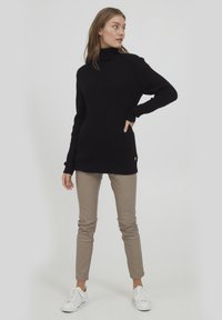 Pull en maille noire avec col roulé et texture côtelée, associé à un pantalon slim beige et des baskets blanches. Look décontracté, peu de détails.