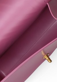 Interno della borsa a tracolla in pelle rosa con texture liscia, con chiusura in metallo color oro e un design pulito e minimalista.