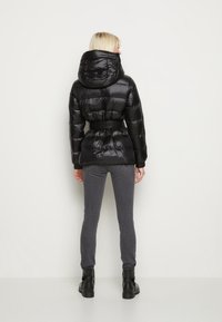 Sort dynejakke med hætte og bælte, der har et quiltet design. Kombineret med grå slim-fit bukser og sorte ankelstøvler.