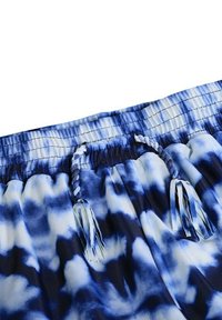 Bañador corto con tintado anudado azul, con cintura de cordón, que presenta una textura suave y lisa y una mezcla de patrones en azul oscuro y claro.