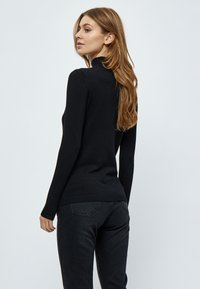 Črna pletena jopica z dolgimi rokavi, turtleneck dizajn, prilegajoč silhuet, rebrast rob in teksturirana tkanina. Nosi se z temnimi kavbojkami.