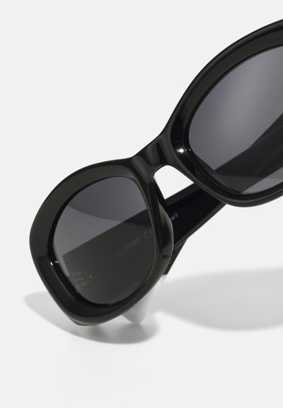 Óculos de sol pretos com grandes armações arredondadas, feitos de plástico brilhante. Lentes escuras com uma textura suave e branding discreto na têmpora.