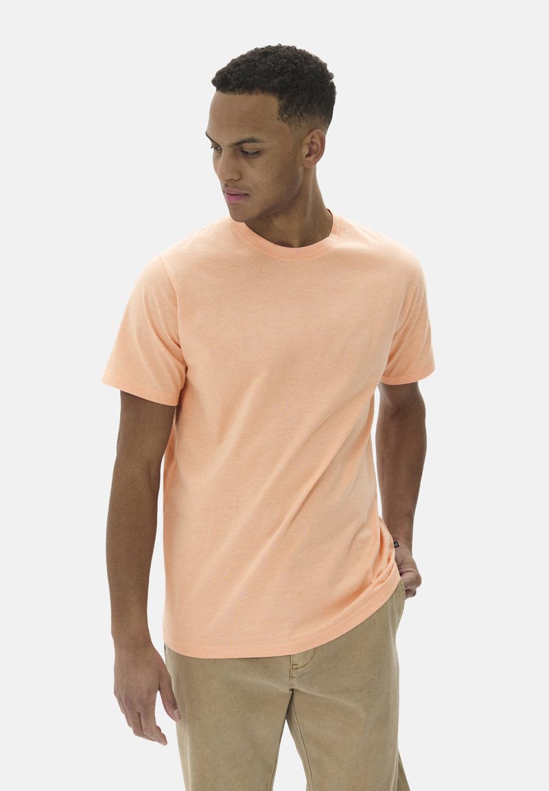 Hellorange T-Shirt mit kurzen Ärmeln aus weichem Stoff, Rundhalsausschnitt, kombiniert mit beigen Hosen. Minimalistisches Design, ohne Muster.