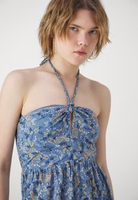 Modra cvetna obleka s halter vratom, ki ima vozlan detajl na sprednjem delu, nabran pas in subtilen paisley vzorec v različnih barvah.