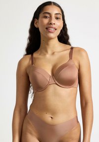 Reggiseno color beige chiaro con una texture liscia simile alla seta, supporto con ferretto e spalline regolabili, abbinato a un slip in stile bikini coordinato.