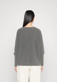 Maglione grigio a maglia con vestibilità rilassata, scollatura arrotondata e lunghe maniche. Presenta una trama a coste e dettagli ai polsini, abbinato a pantaloni color crema.