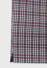 Gros plan sur un tissu avec une petite fente latérale, présentant un motif à carreaux en noir, blanc, rose et marron.