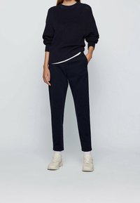 Granatowy sweter dzianinowy z okrągłym dekoltem i opuszczanymi ramionami, zestawiony z ciemnymi spodniami i jasnymi trampkami. Gładka tkanina o luźnym kroju.