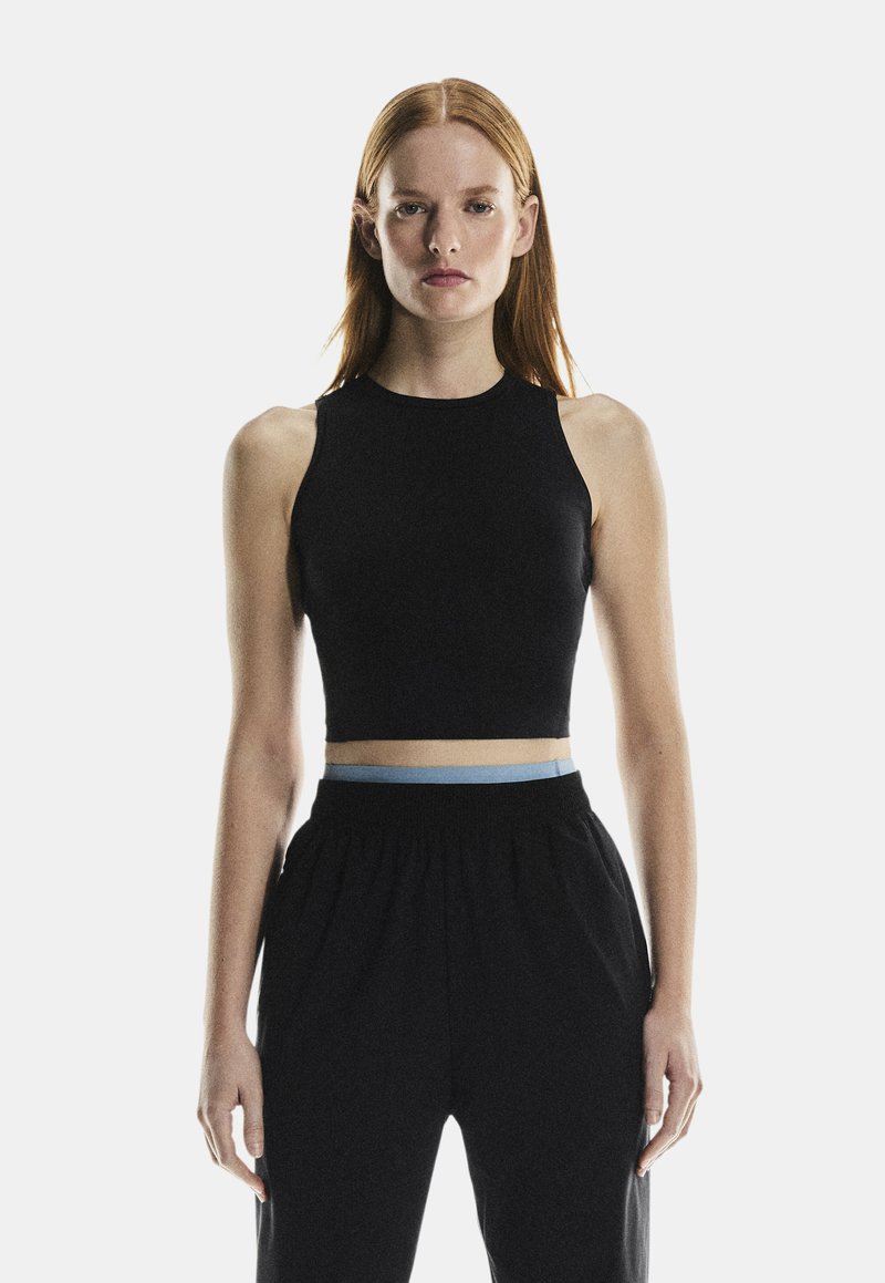 Un crop top noir sans manches avec un col montant, doté d'une ceinture contrastante bleu clair, associé à un pantalon noir ample.