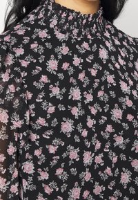 Black floral blouse with pink and white roses, featuring a pleated high collar and sheer, textured fabric. Design includes small leaf accents.