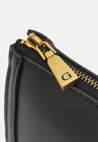 Eckige schwarze Lederhandtasche mit goldfarbenem Reißverschluss, ausgestattet mit einem rechteckigen Reißverschlussanhänger, der mit einem "G" geprägt ist, und einem strukturierten Stofffutter.