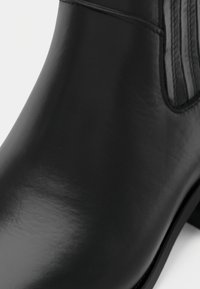 Černá kotníková bota z kůže s hladkým, lesklým povrchem, s žebrovanými detaily a nízkým blokovým podpatkem. Design je elegantní a minimalistický.