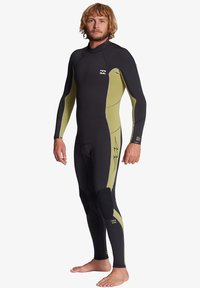 Full-body wetsuit in black with olive green accents, featuring a smooth texture, long sleeves, knee pads, and a small logo on the chest.