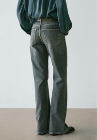 Džínové kalhoty s rozšířenými nohavicemi v bledém šedém odstínu s klasickým pětiprvkovým designem kapes a jemnými švy, doplněné volným zeleným topem.