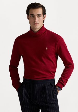 Rode coltrui gemaakt van zachte stof, met een klein geborduurd logo op de borst. Gemaakt in combinatie met marineblauwe gestreepte broeken.