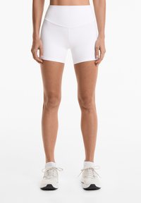 White fitted athletic shorts with a high waistband, smooth texture, and mid-thigh length, paired with light-colored running shoes.