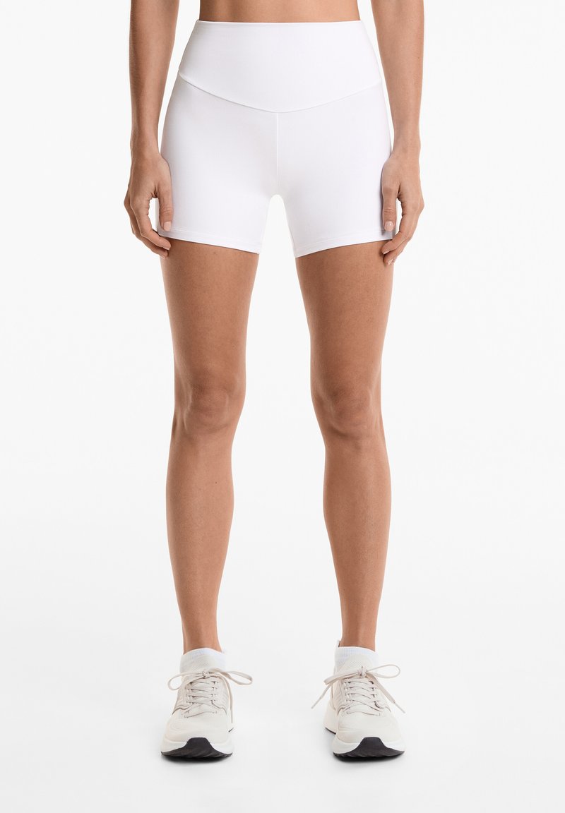 White fitted athletic shorts with a high waistband, smooth texture, and mid-thigh length, paired with light-colored running shoes.