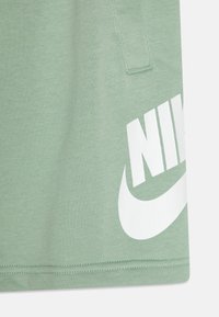 Grønn bomullsblanding med teksturert overflate, med en stor hvit "Nike"-logo og swoosh-design på nederste høyre side.
