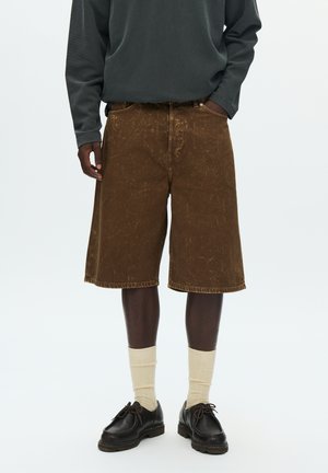 Brown denim shorts with a relaxed fit, featuring subtle texture. Paired with cream-colored socks and dark shoes.