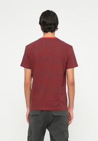 Rød og marineblå striped t-skjorte med rund hals og korte ermer, laget av mykt stoff. Bakdelen har et rent, enkelt design.