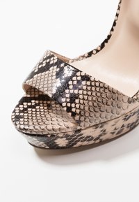 Des sandales à talons hauts présentant un motif en serpent noir et beige, une texture brillante, un large design de brides croisées et une semelle compensée.