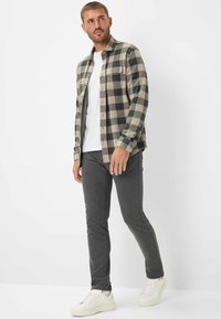 Camicia di flanella a quadri beige e nera, indossata sopra una t-shirt bianca, abbinata a pantaloni grigi e sneakers bianche.