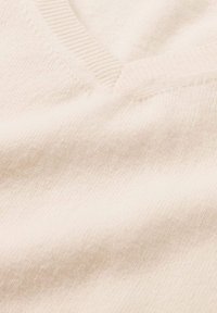 Cremefarbener Strickstoff mit V-Ausschnitt, weicher Textur und gerippten Kanten. Keine erkennbaren Muster oder Hardware sichtbar.