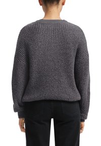 Grijze gebreide trui met een gestructureerd patroon, gedropte schouders en geribbelde manchetten, gecombineerd met zwarte jeans. De achterkant toont een ontspannen pasvorm.