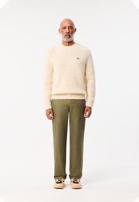 Crème gekleurde trui met een ronde hals, olijfgroene broek en tan sneakers met dierlijke prints.